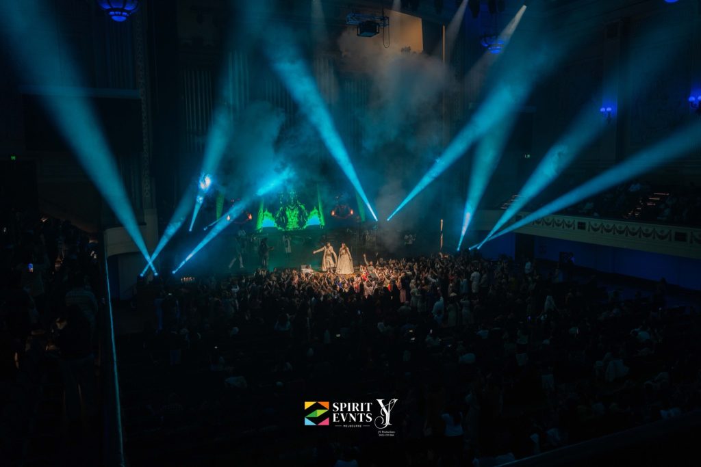 High-angle view of the packed floor of Melbourne Town Hall with blue spotlight beams cutting through haze at Bhajan Clubbing