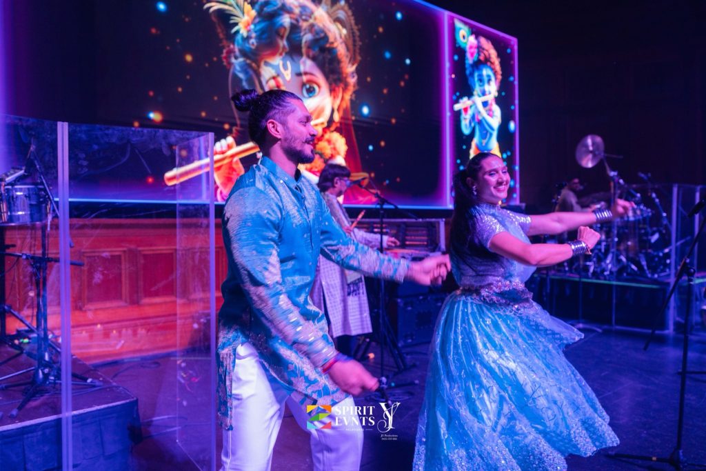 Two dancers in coordinated blue traditional outfits performing on stage in blue and purple light at Bhajan Clubbing, Melbourne Town Hall