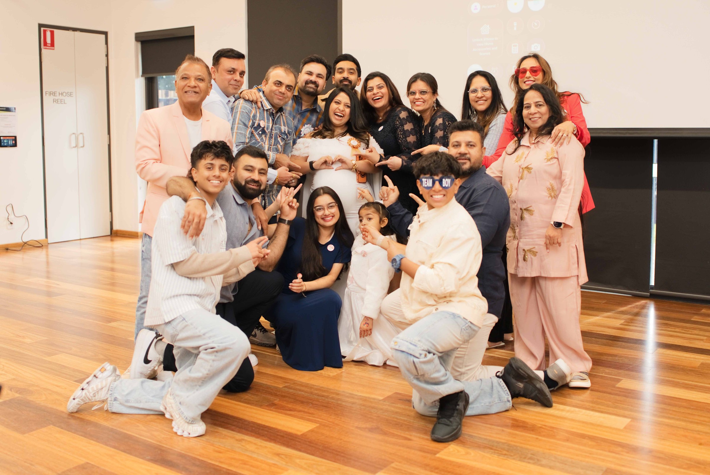 A large group of family and friends gathered around Honey and Tarak indoors for a group photo