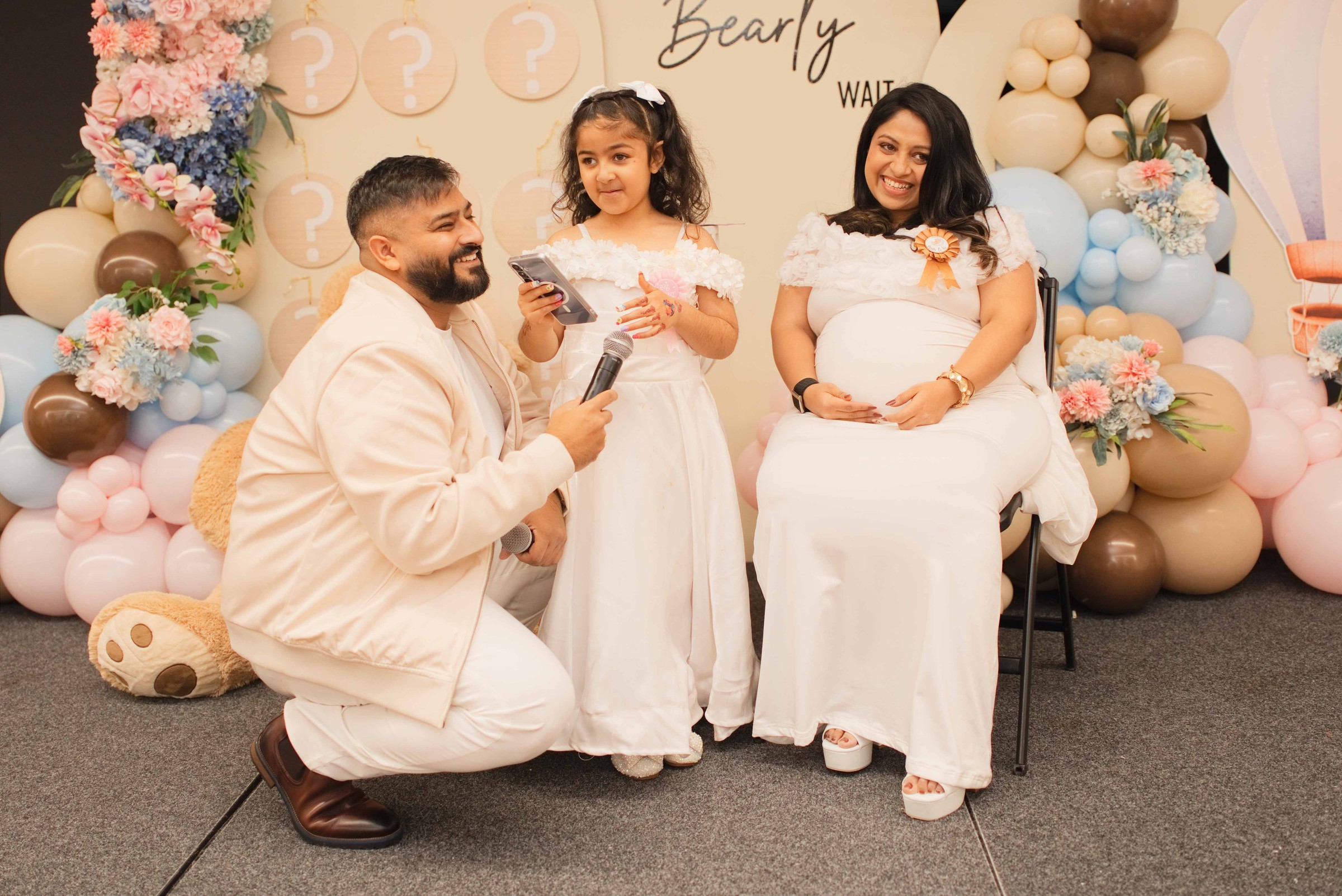 Honey and Tarak in front of the gender reveal backdrop with a young girl