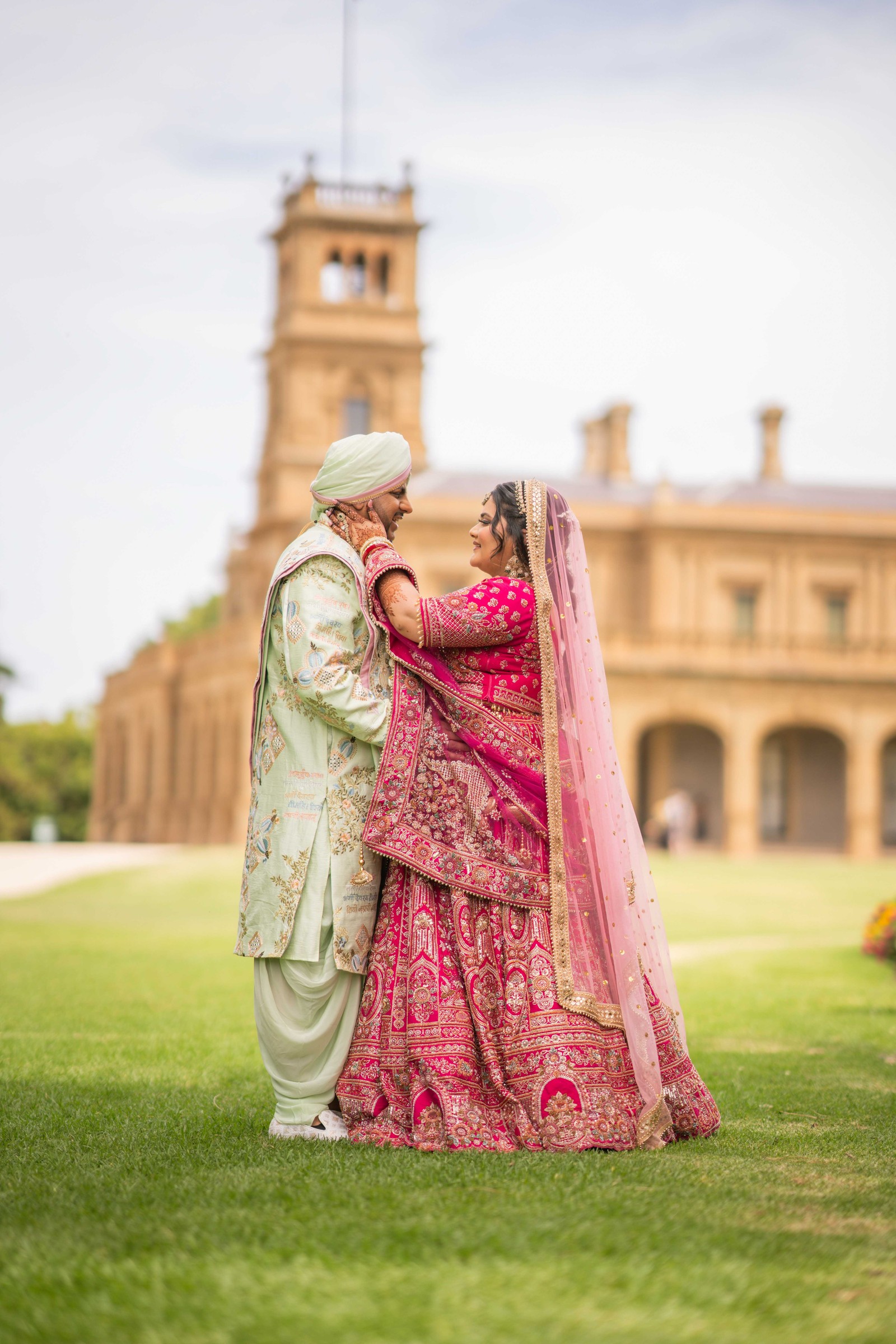 Jatin and Aman holding hands and facing each other on the lawn, with a stone tower behind them