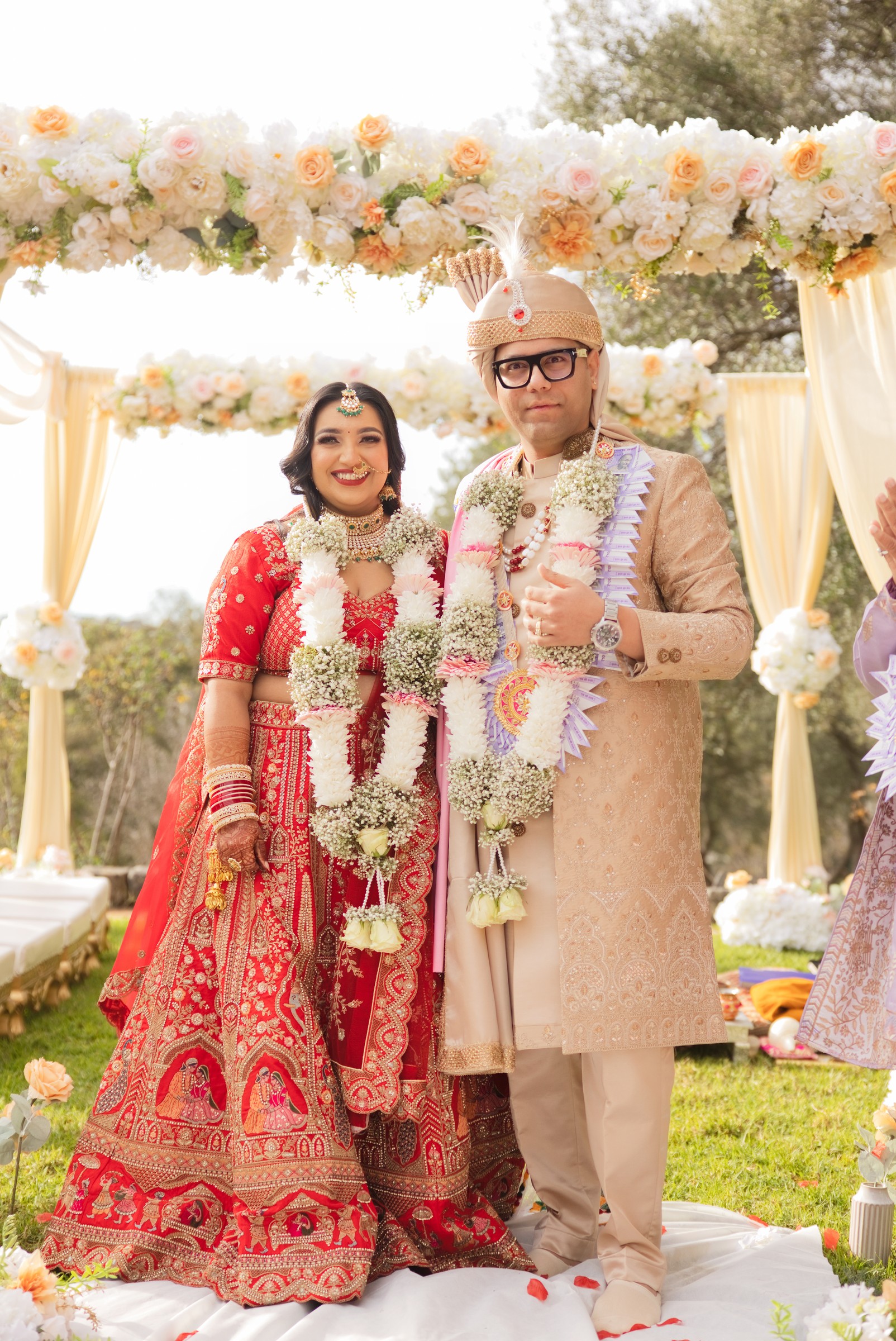 Jay and Ashna standing together under a mandap decorated with white and pink roses