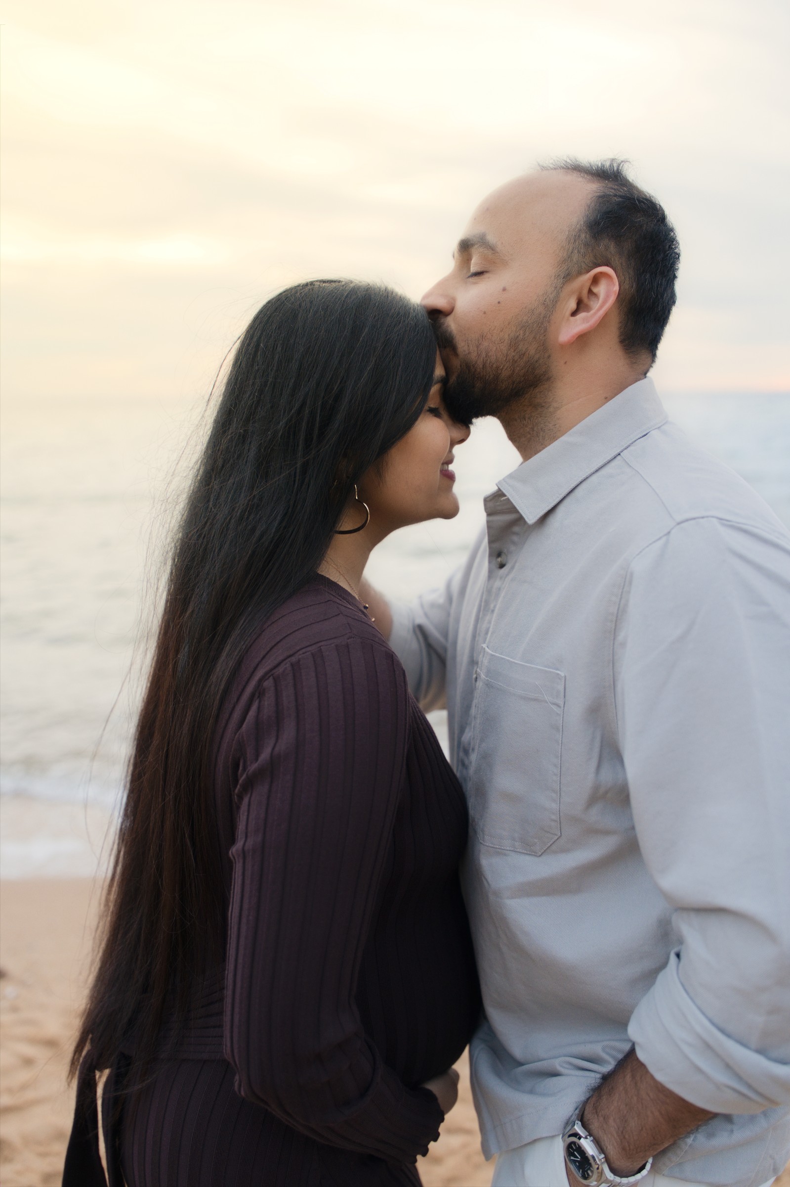 Maulik gently kissing Madhvi's forehead during their beach maternity session