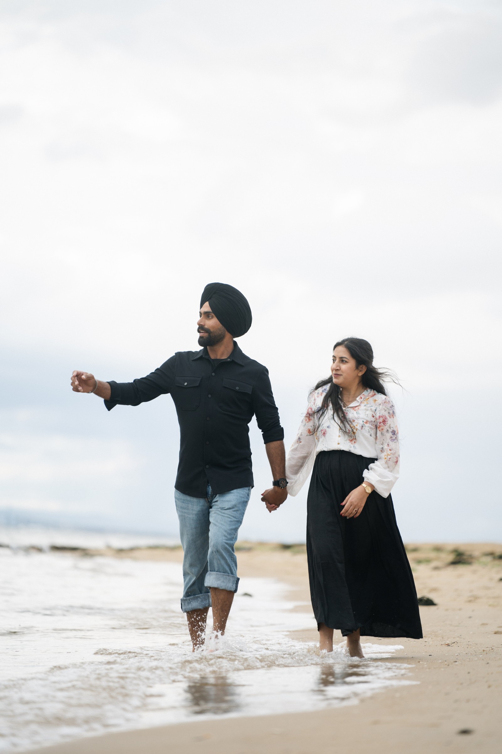 Ravi and Rav holding hands and walking barefoot in the shallow surf