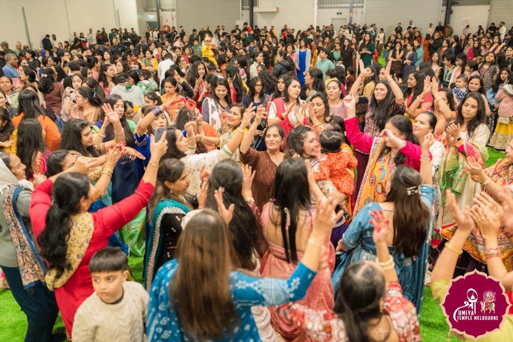 High-angle view of many people in colourful saris and lehengas dancing with raised hands in the hall at a Janmashtami celebration in Melbourne