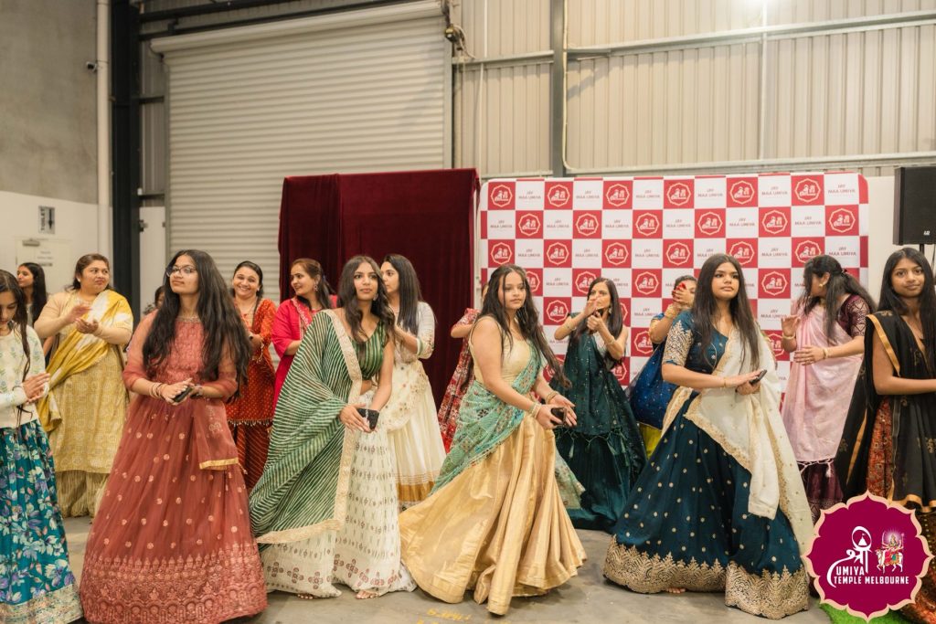 Women in colourful lehengas dancing in a line in front of a red and white backdrop at a Janmashtami celebration in Melbourne